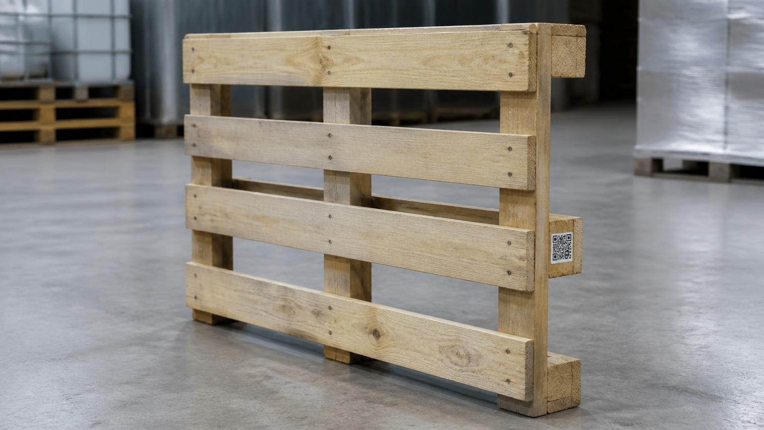 A plain wooden shipping pallet on a warehouse floor with a small unbranded identity tag fixed to its stringer board.